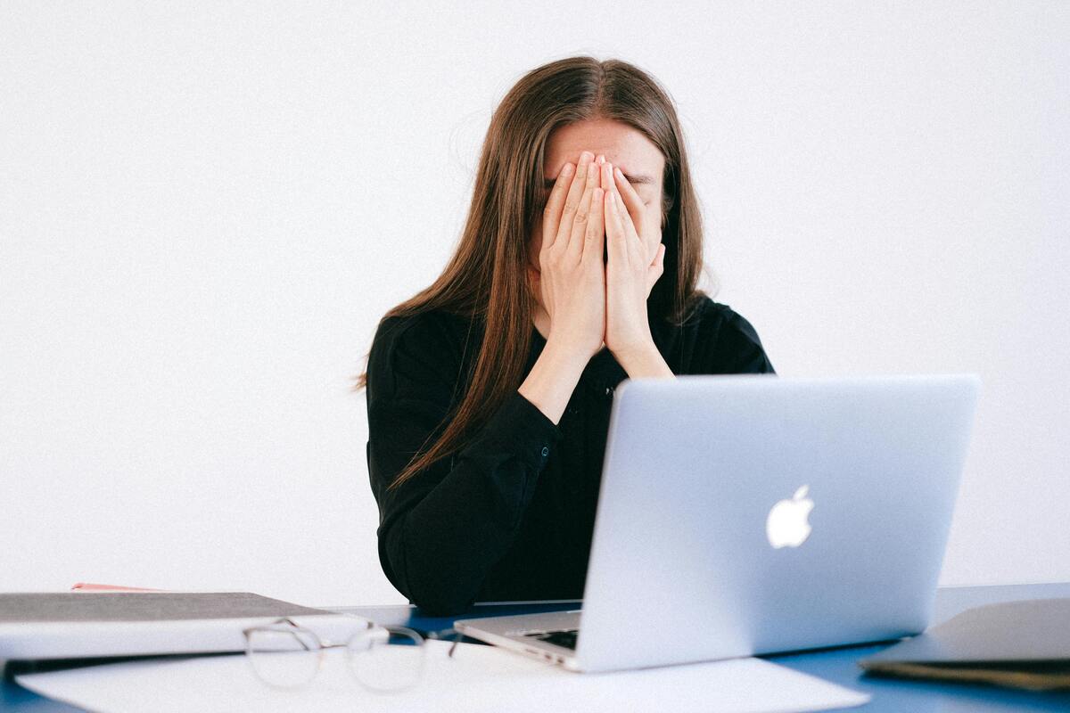 young woman at a computer holding her face in her hands, apparently stressed