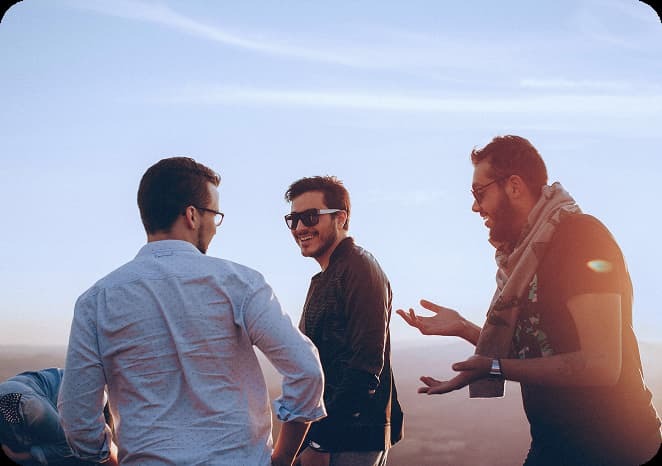Three young men standing outdoors at sunset, smiling and talking together